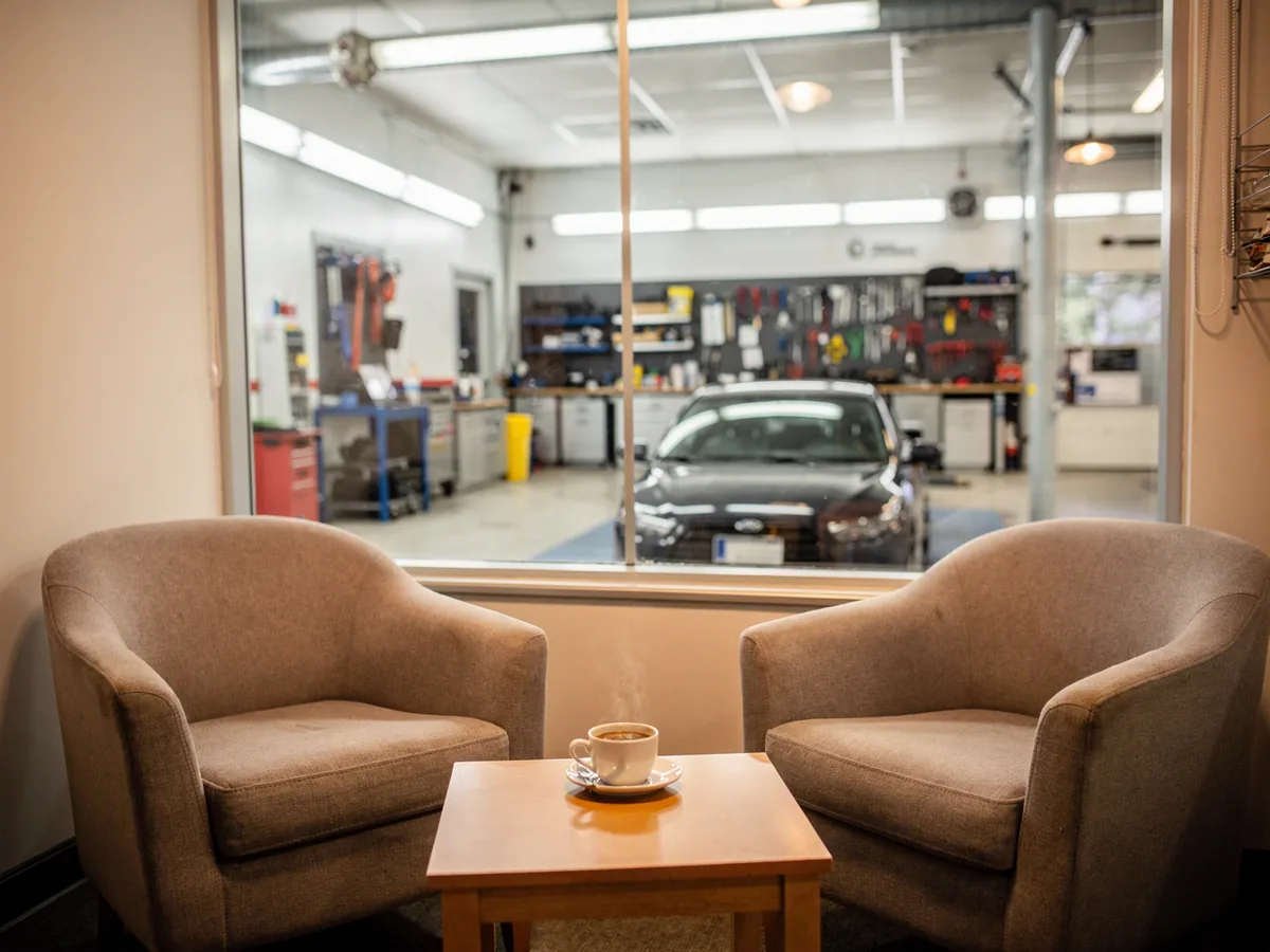 A cozy waiting lounge with coffee and a glass wall to the workshop